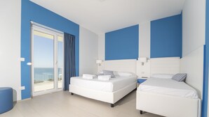 Un dormitorio moderno con dos camas, un amplio ventanal corredero a un balcón y vista al mar.