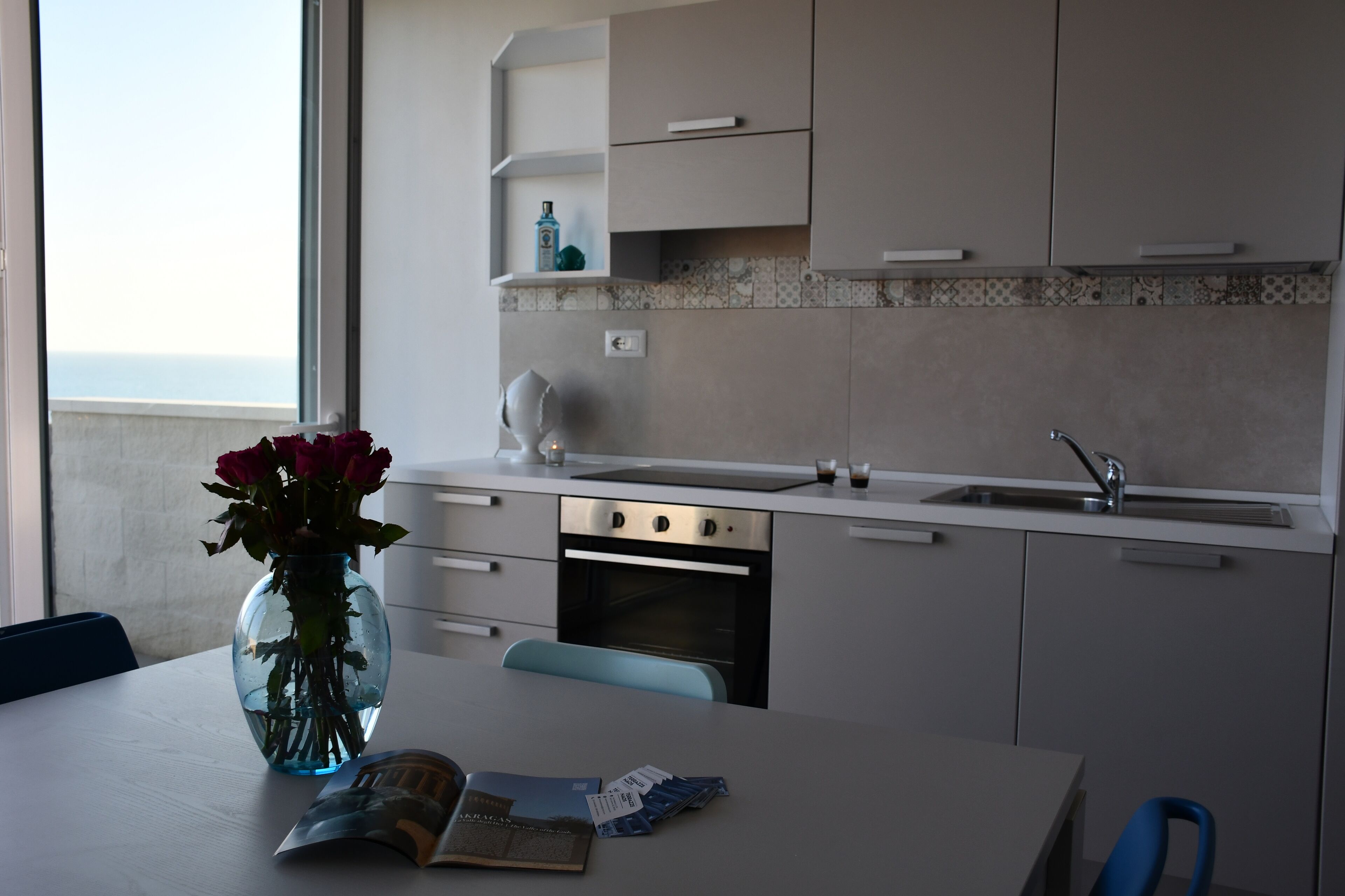Et moderne køkken med en hvid bordplade, en vask og et indbygget ovn. Der står en vase med blomster på bordet.