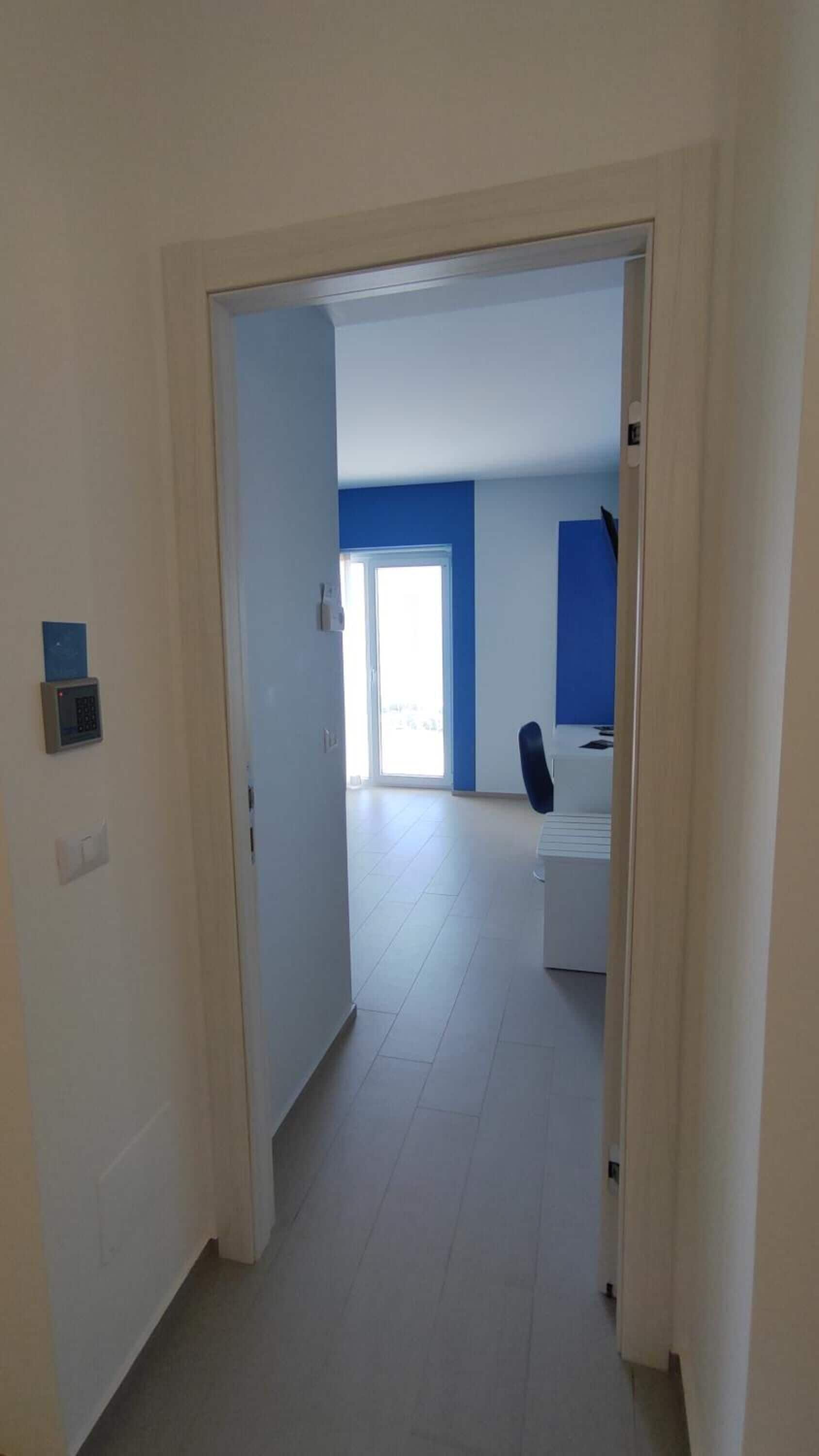 A hallway leading to a bedroom with a bed, a chair, and a window.