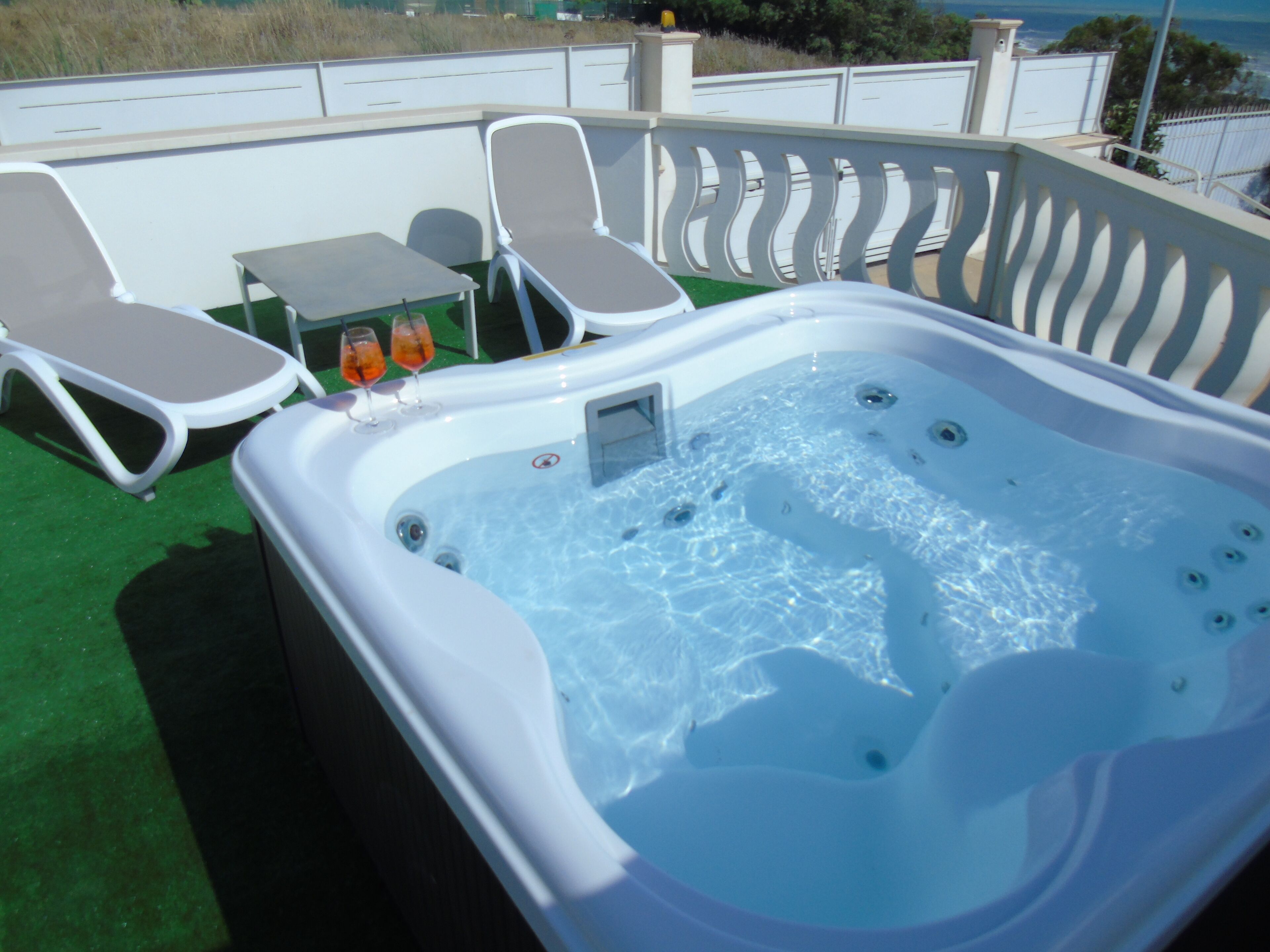 Een hottub met twee loungestoelen en een klein tafeltje, omringd door een witte reling.