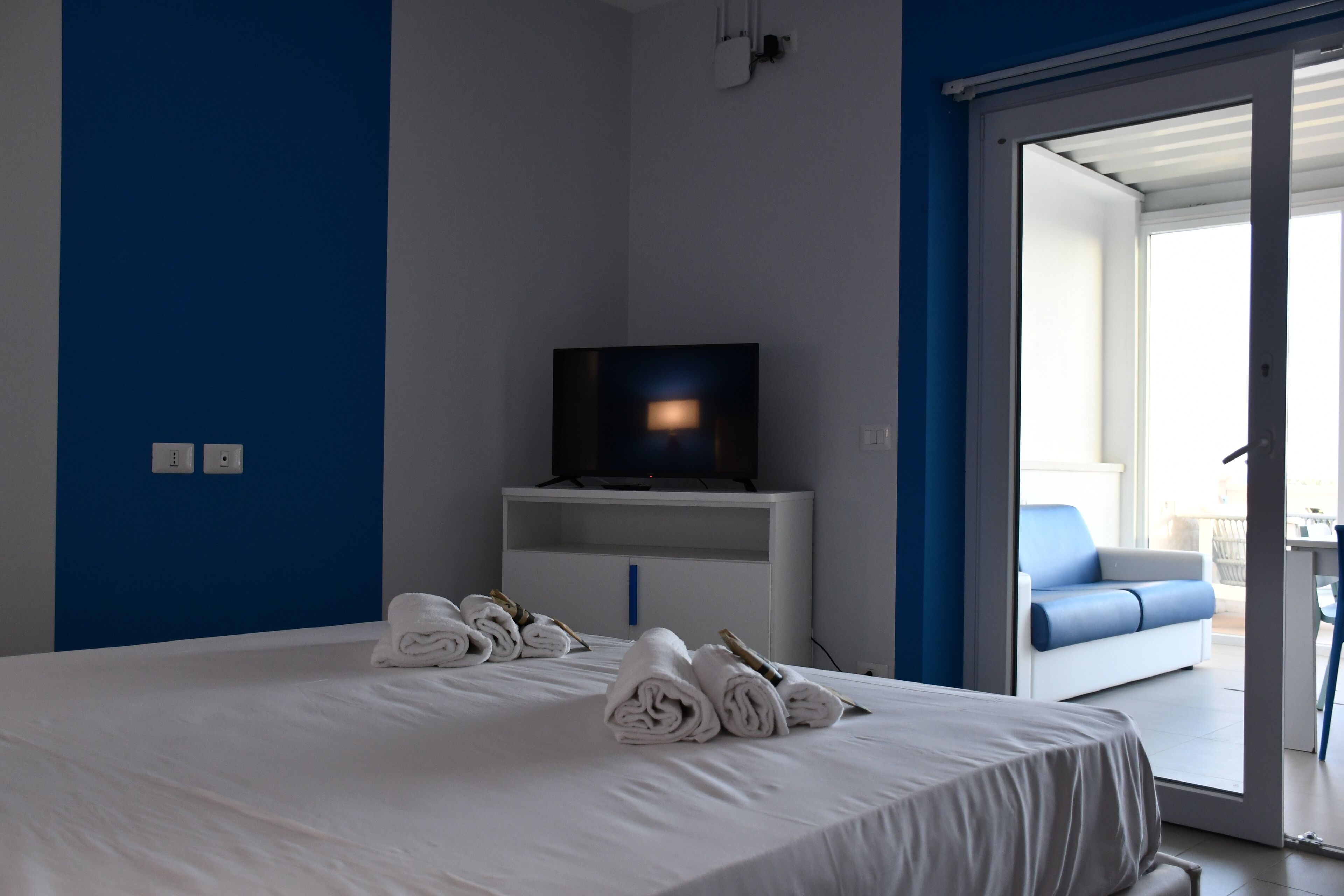 Ein Hotelzimmer mit Bett, Fernseher auf einem Schrank und Blick auf den Balkon.