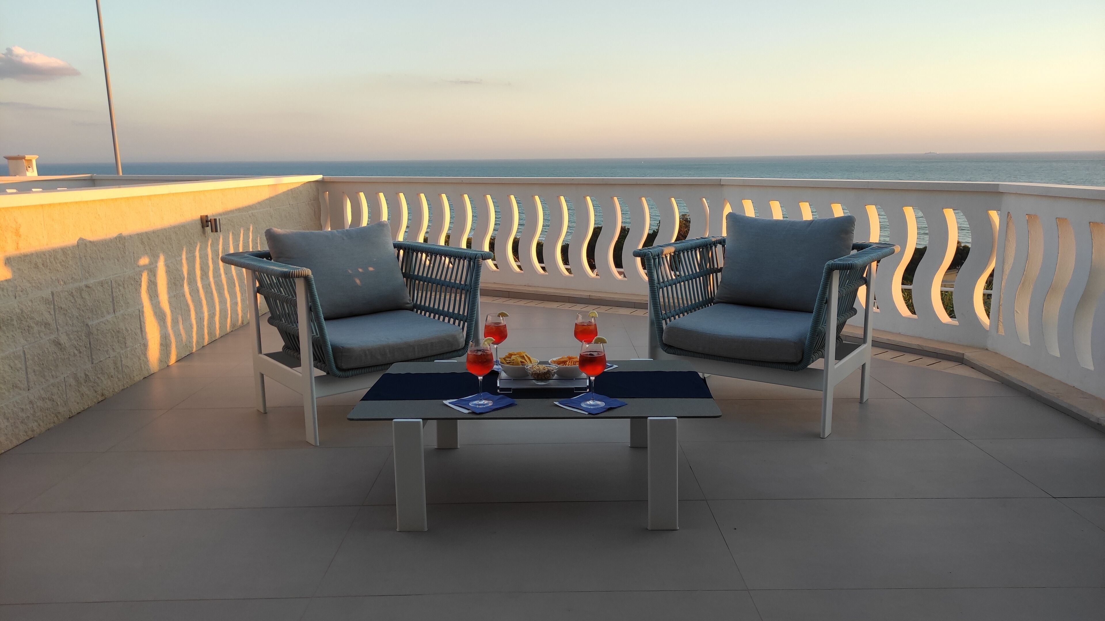 Ein Balkon mit zwei Korbstühlen, einem Tisch und Blick aufs Meer.