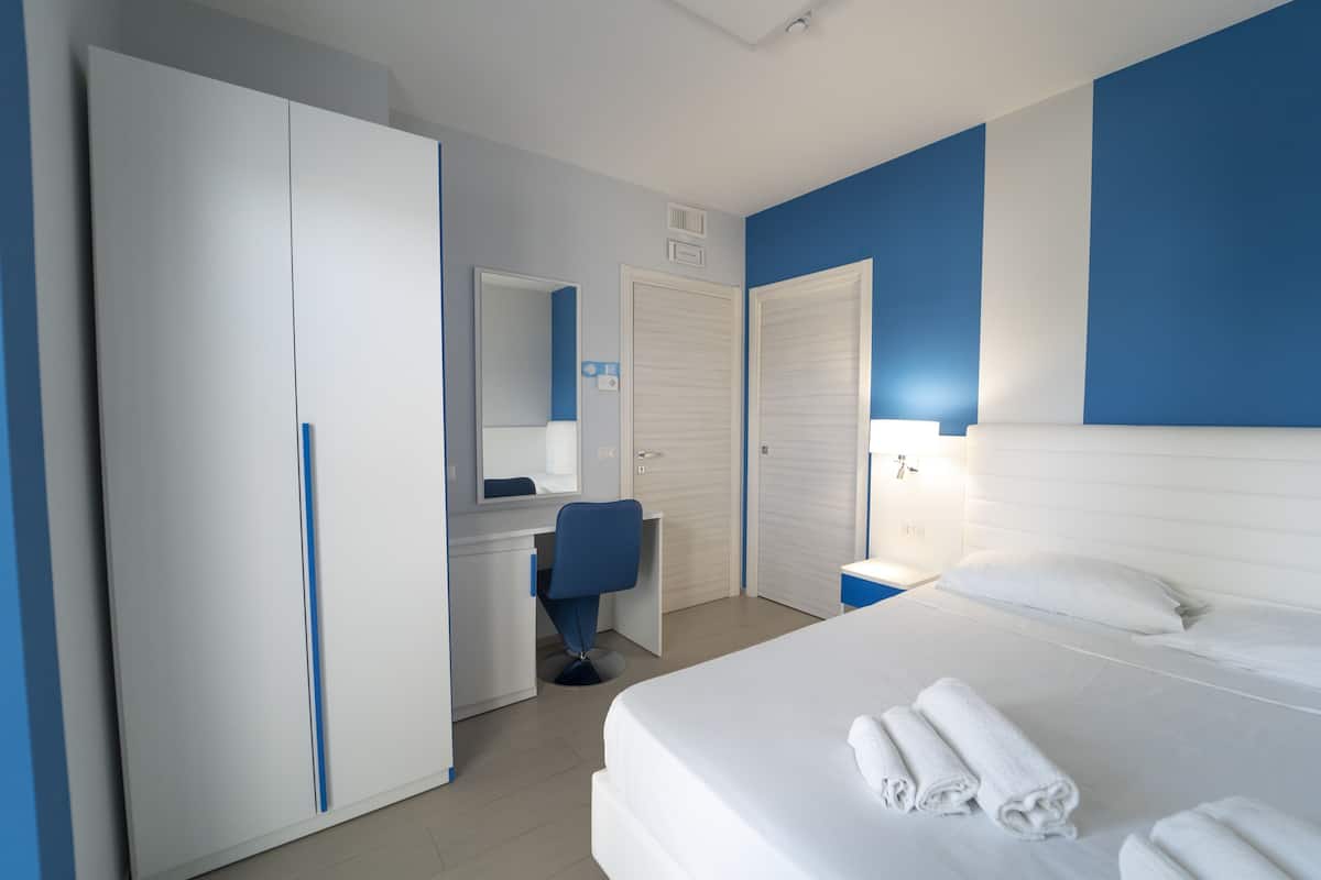 A hotel room with a bed, a desk, a chair, and a wardrobe.