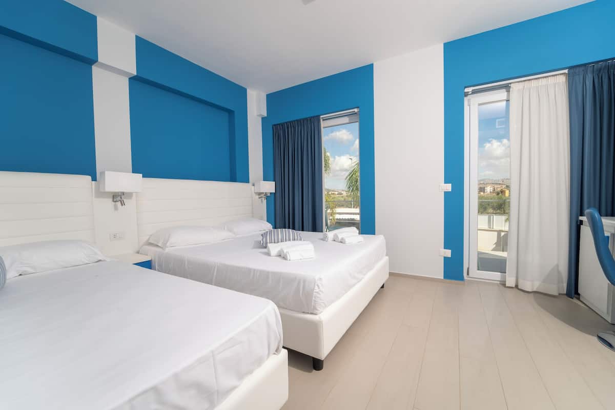 A hotel room with two beds, a large window with curtains, and a view of the outside.