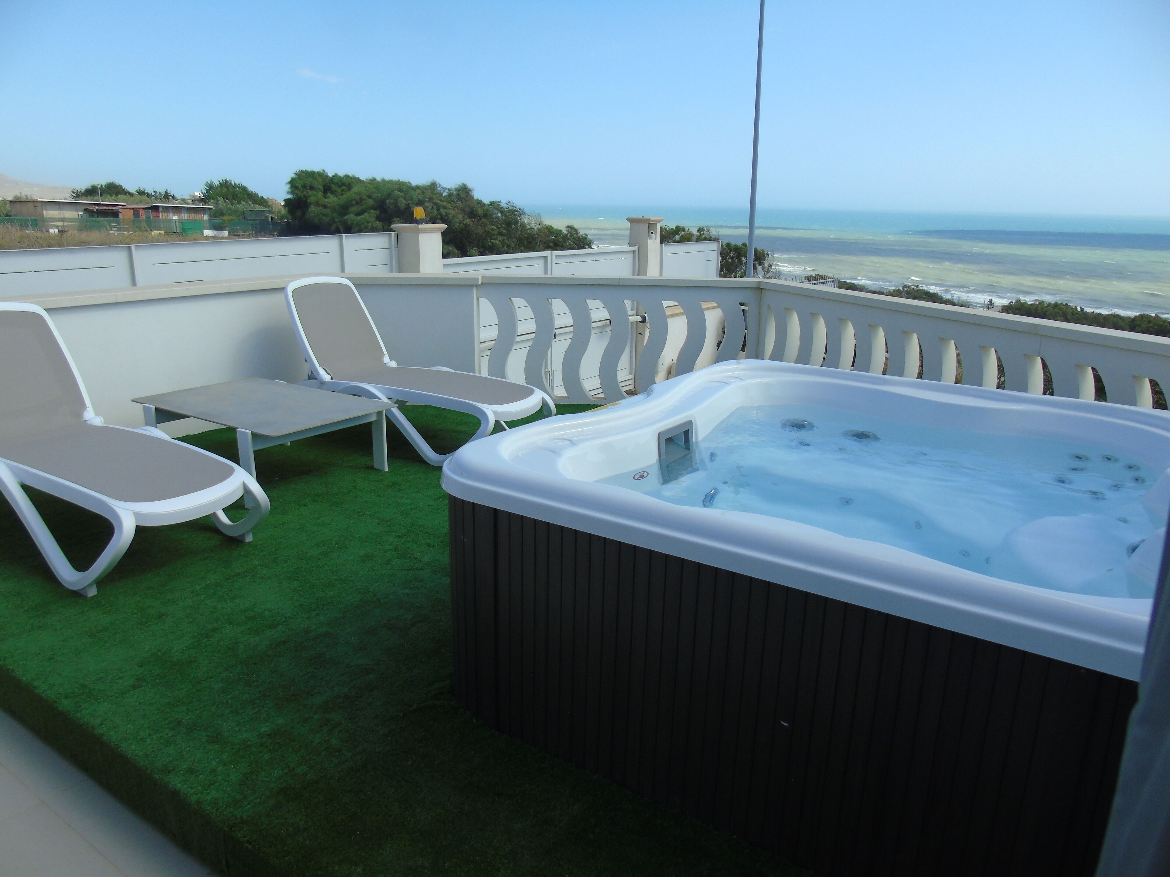 Een balkon met twee witte loungestoelen, een tafeltje en een jacuzzi.