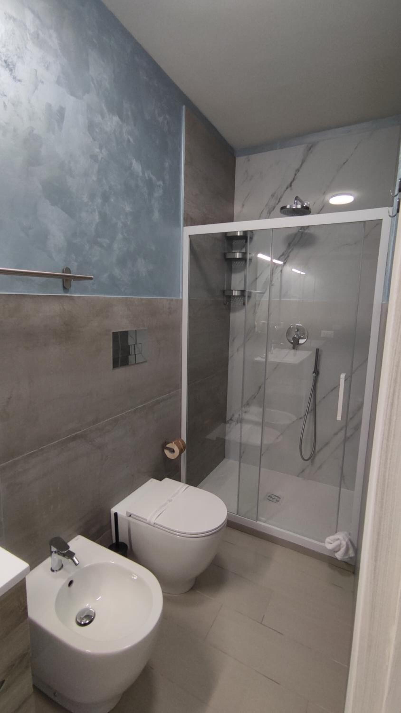 Een moderne badkamer met een douchecabine van glas, een wit toilet en een bidet.