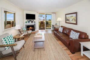 A living room with a fireplace, a television, a sofa, and a view through the glass doors. - Desired D building with great south facing views and just steps to the sand. D102 NCV (Oceanside)