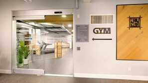 L’entrée d’une salle de sport, avec une porte en verre, un tapis de course et du matériel d’exercice.