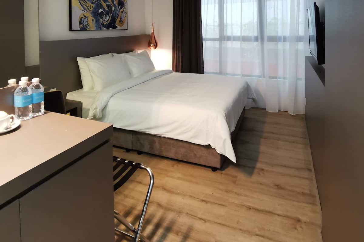Ein Hotelzimmer mit Bett, Schreibtisch mit Wasserflaschen, einem Bild an der Wand, einem Fernseher und einem Fenster mit Vorhängen.