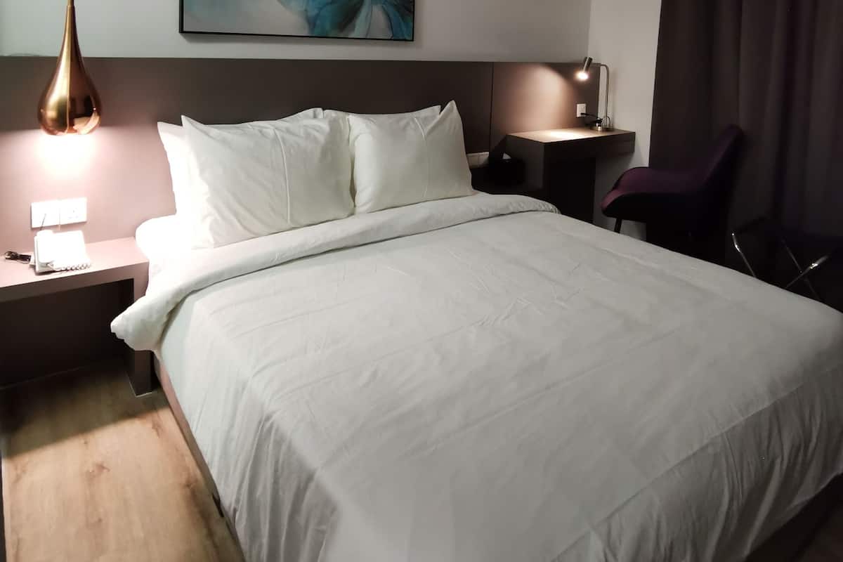 Ein modernes Hotelzimmer mit einem großen Bett, einem Nachttisch mit Lampe, einem Schreibtisch mit Stuhl und einem großen, abstrakten Gemälde an der Wand.