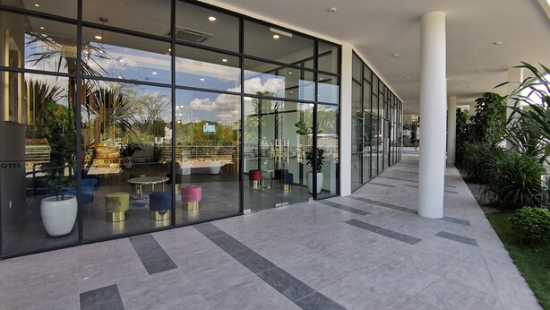 A modern hotel lobby with large glass windows, outdoor seating, and potted plants. - Otel Hotel Sibu (Sibu)