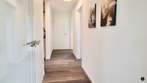A hallway with wooden flooring, white walls, and modern lighting fixtures. - Refugium 4 (Kellenhusen)