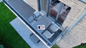 A modern outdoor patio with a dining table, chairs, and a glass railing. - Refugium 4 (Kellenhusen)