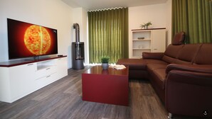 A modern living room with a flat-screen TV, a brown leather sofa, a red coffee table, and a green curtain. - Refugium 4 (Kellenhusen)