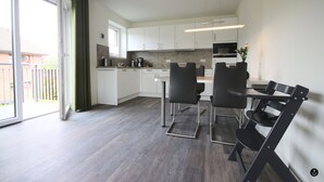 A modern kitchen with white cabinets, a dining area with black chairs, and a sliding glass door to the outside. - Refugium 4 (Kellenhusen)