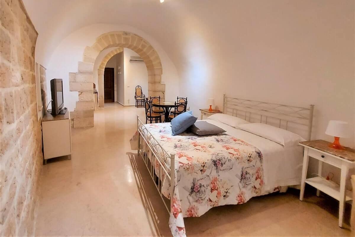 Un dormitorio con cama, televisor, escritorio y silla. Se ve una escalera que conduce a otra habitación.