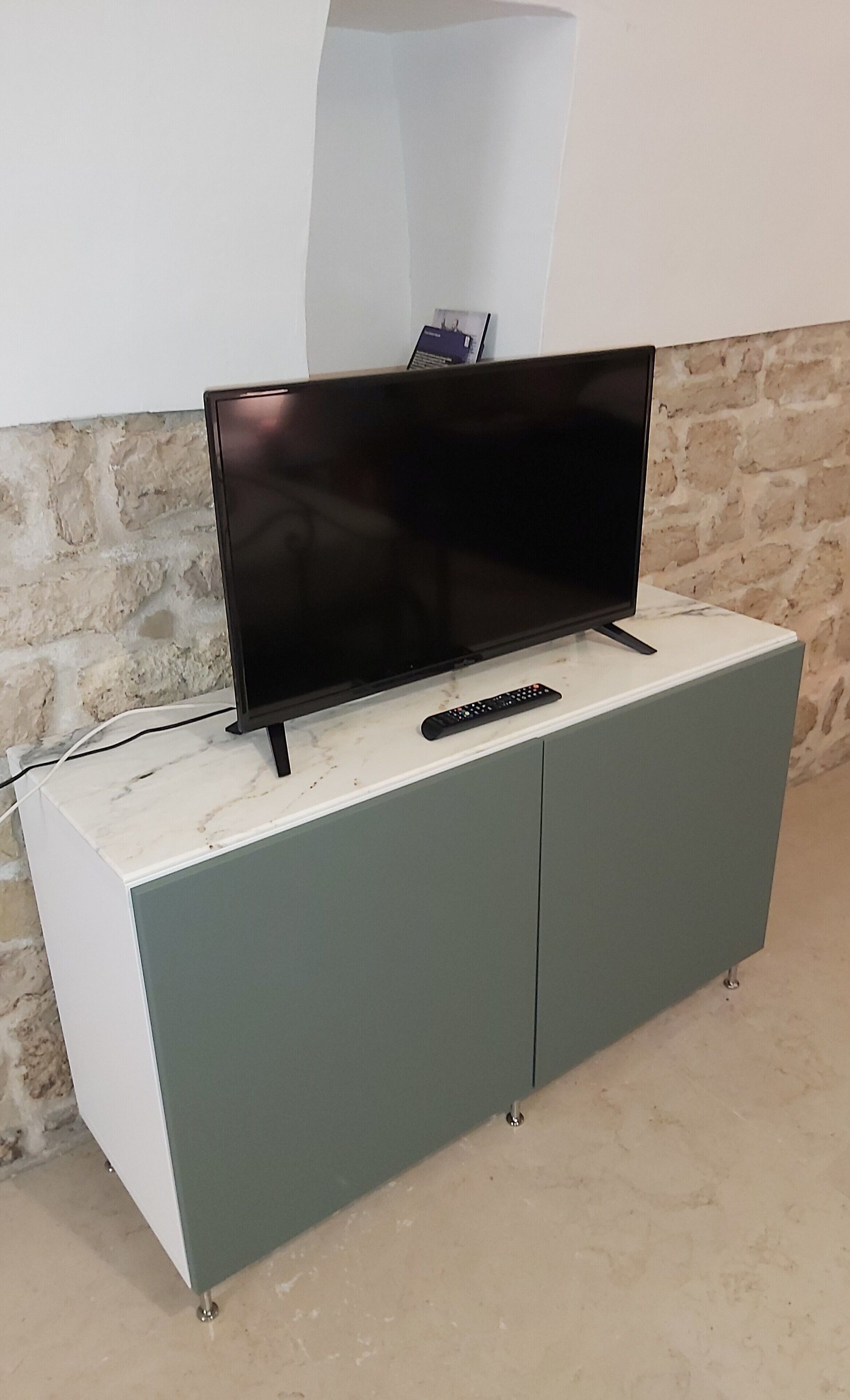 Un televisore a schermo piatto su un mobiletto bianco e verde, con un telecomando accanto.