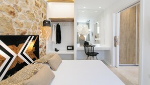 Un dormitorio moderno con pared de piedra, una cama con ropa de cama color beige, un cuadro geométrico blanco y negro en la pared, una silla negra y una puerta de madera.