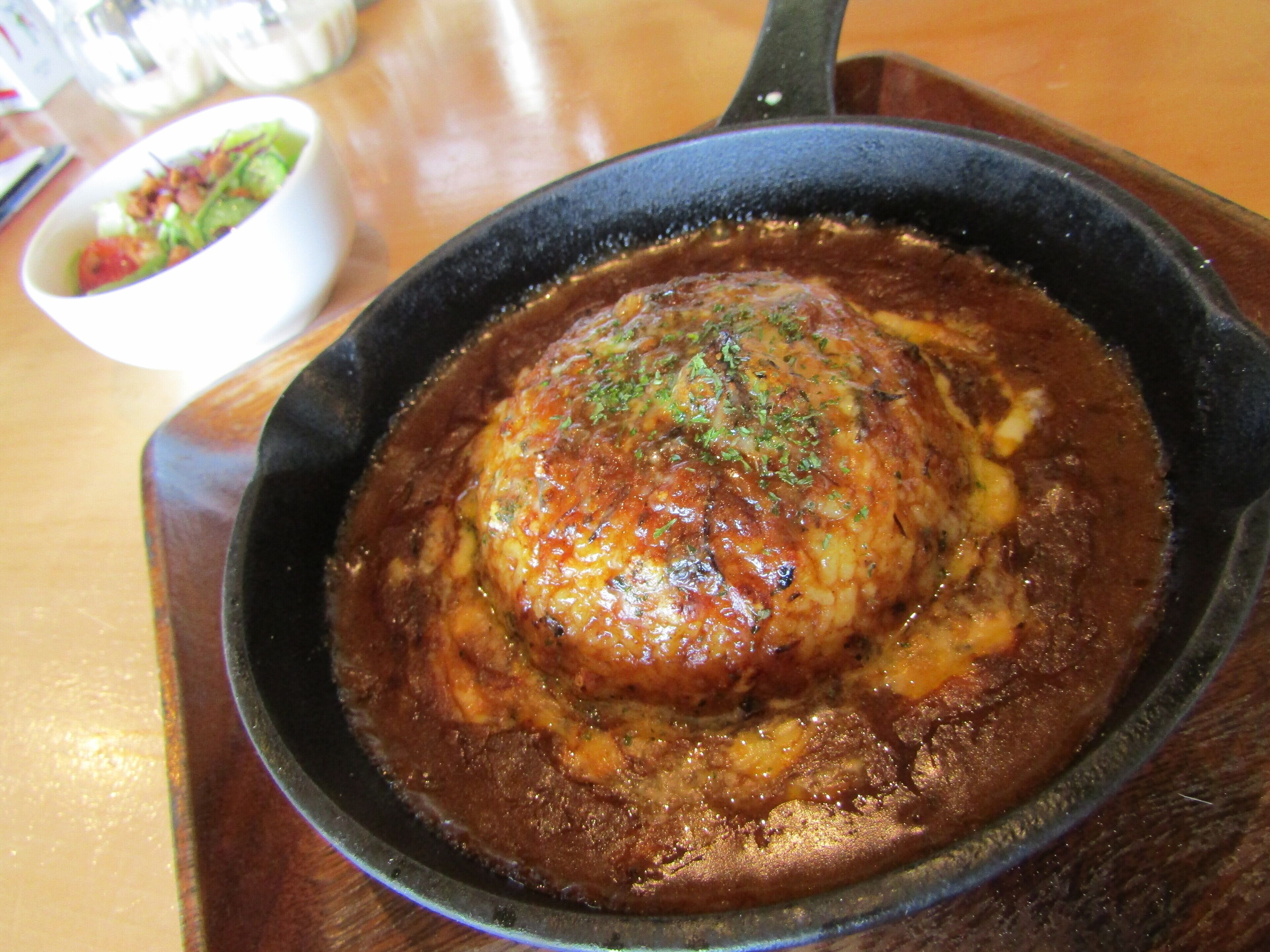 A skillet with a meatball covered in sauce, placed on a wooden table.