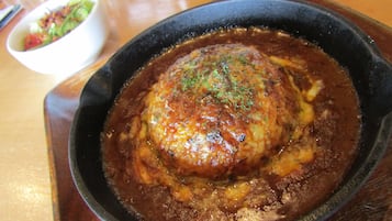 A skillet with a meatball covered in sauce, placed on a wooden table.
