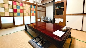 Una habitación japonesa tradicional con suelo de tatami, una mesa de madera, un televisor y un shoji con paneles de colores.