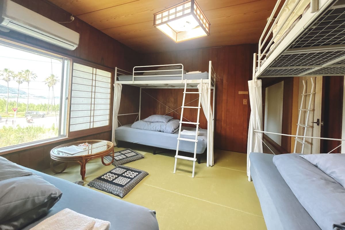 A bunk bed room with a window, a small table, and a sofa.