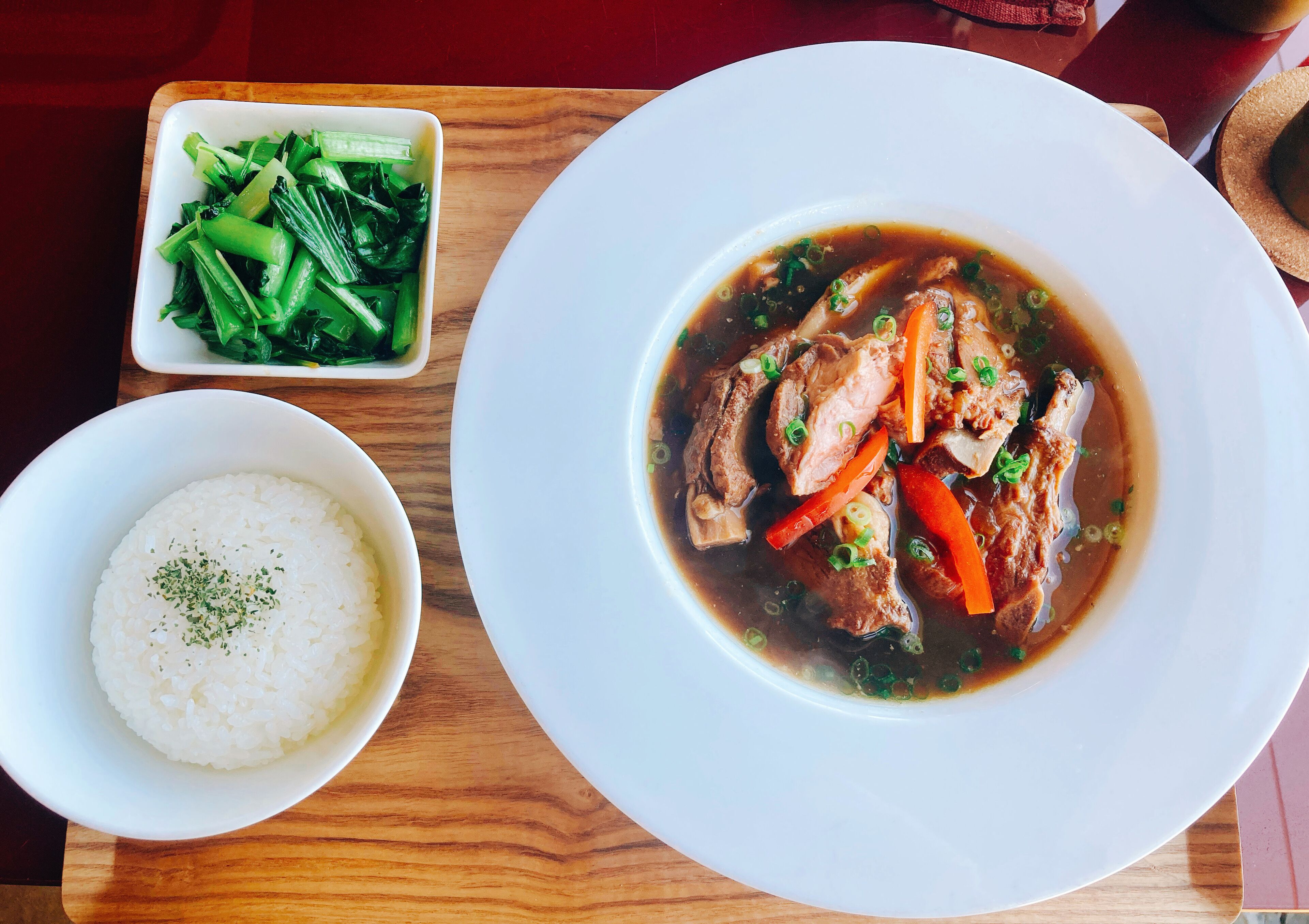 A meal consisting of a bowl of white rice, a bowl of green vegetables, and a plate of soup with meat and vegetables.