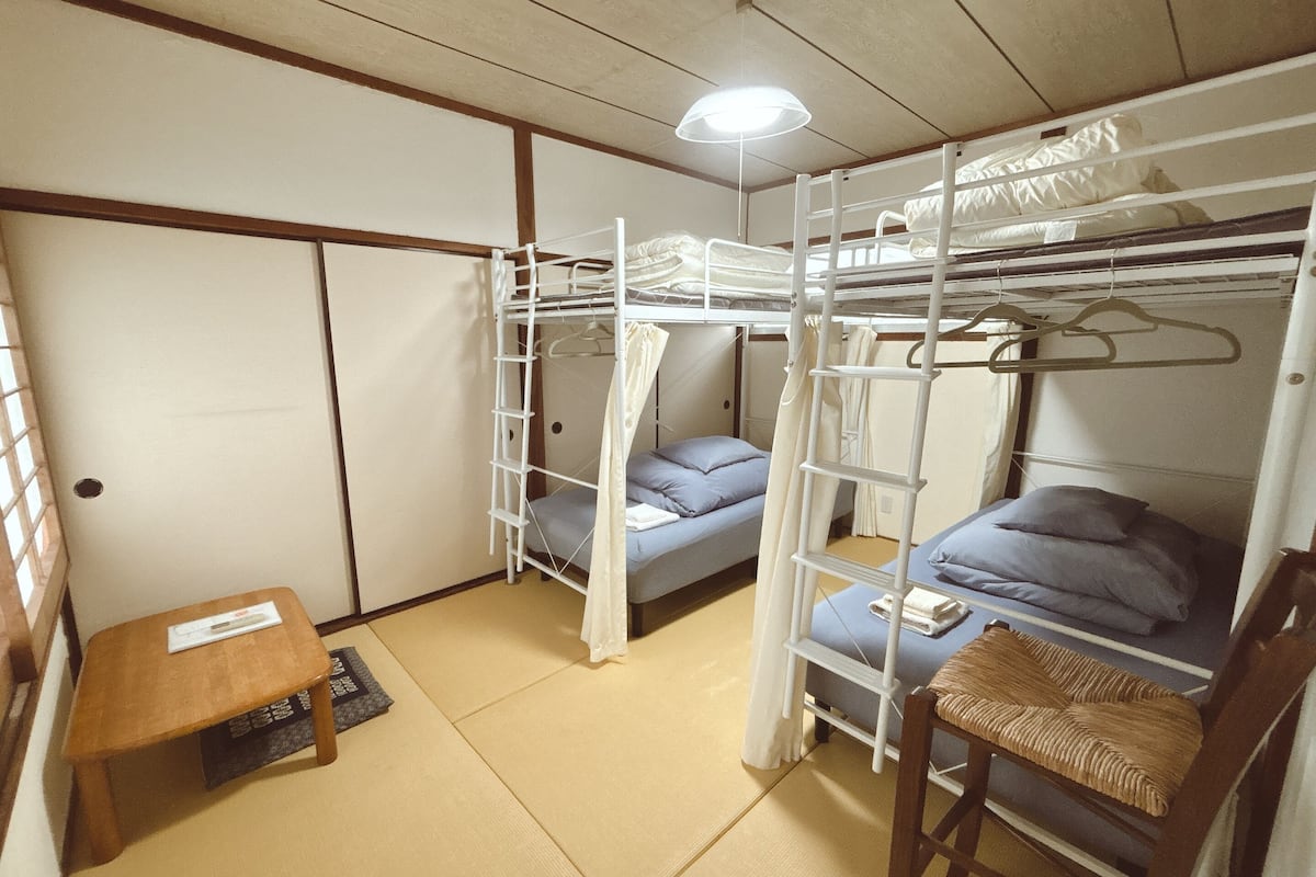 A dormitory room with bunk beds, a small table, and a chair.