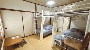 A dormitory room with bunk beds, a small table, and a chair.