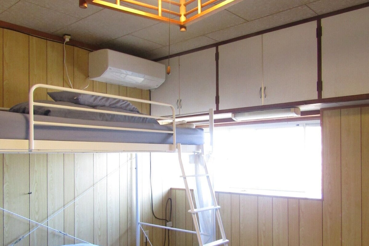A bunk bed room with a ladder, a window, and a small table.