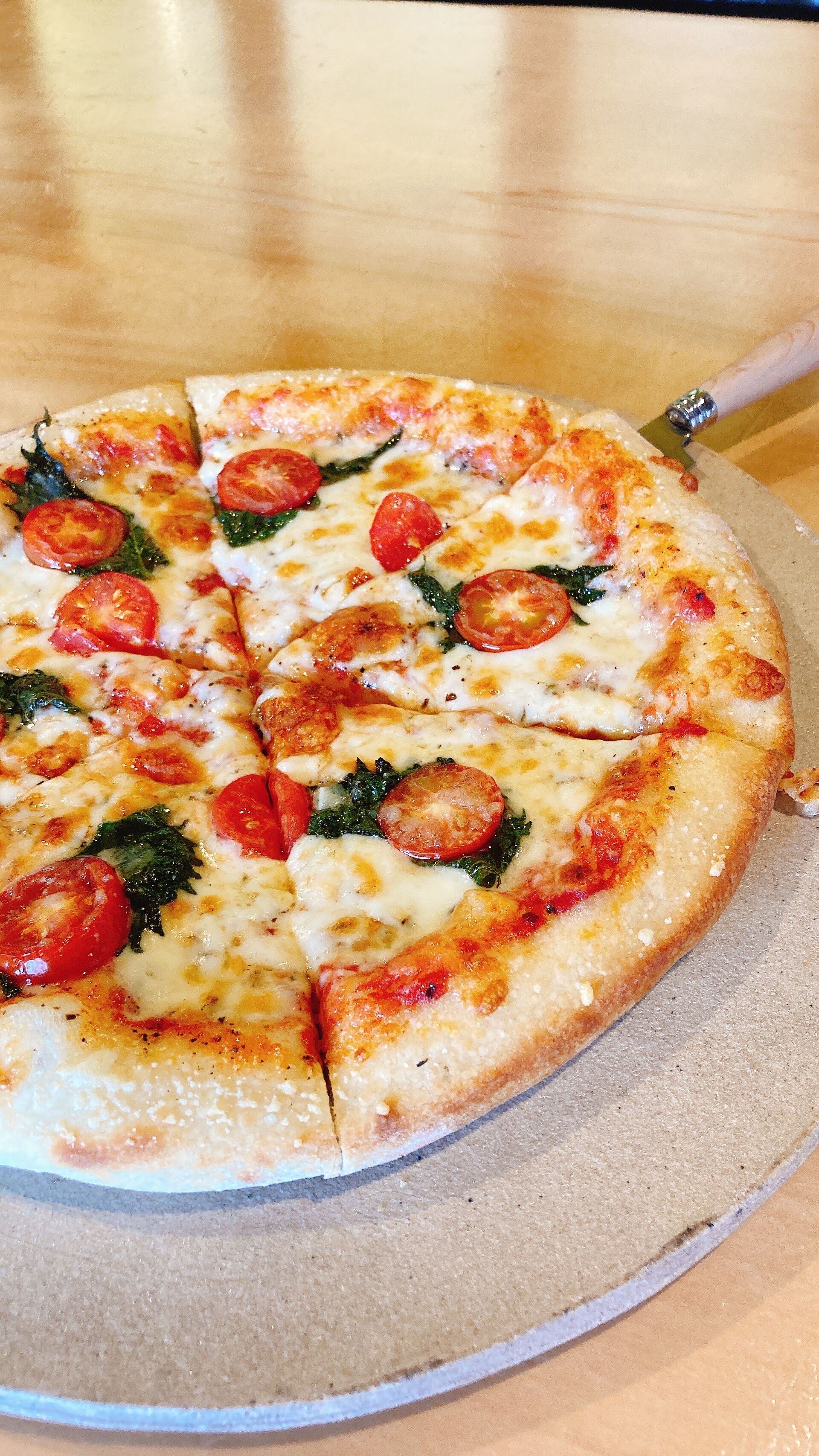 A pizza with tomato slices and greens on a round tray.
