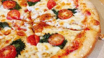 A pizza with tomato slices and greens on a round tray.