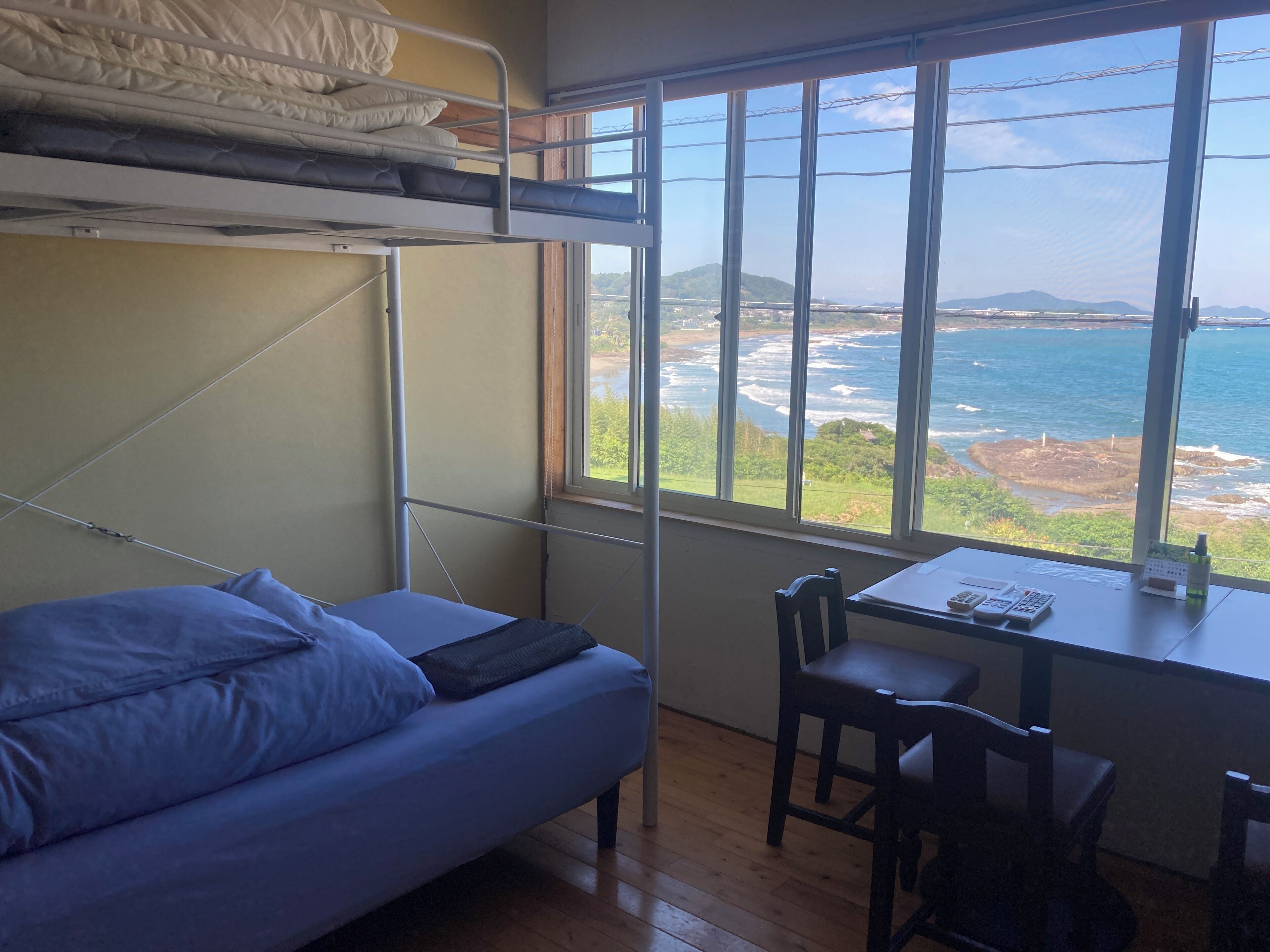 A bunk bed with a view of the sea, a desk with a chair, and a window.