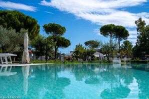 A clear swimming pool with a white umbrella, surrounded by trees and buildings.