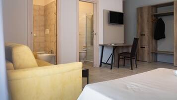 Quarto de hotel com cama, poltrona amarela, escrivaninha com cadeira, televisão fixada na parede e guarda-roupa de madeira.