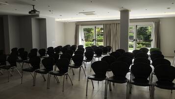 A conference room with rows of chairs, a projector, and large windows with curtains.
