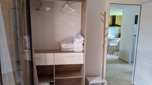 Un armario vestidor con repisas, barra para colgar ropa y un perchero con toallas dobladas.
