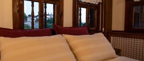 Una cama con almohadas blancas y rojas, marcos de ventana de madera y cortinas de encaje.