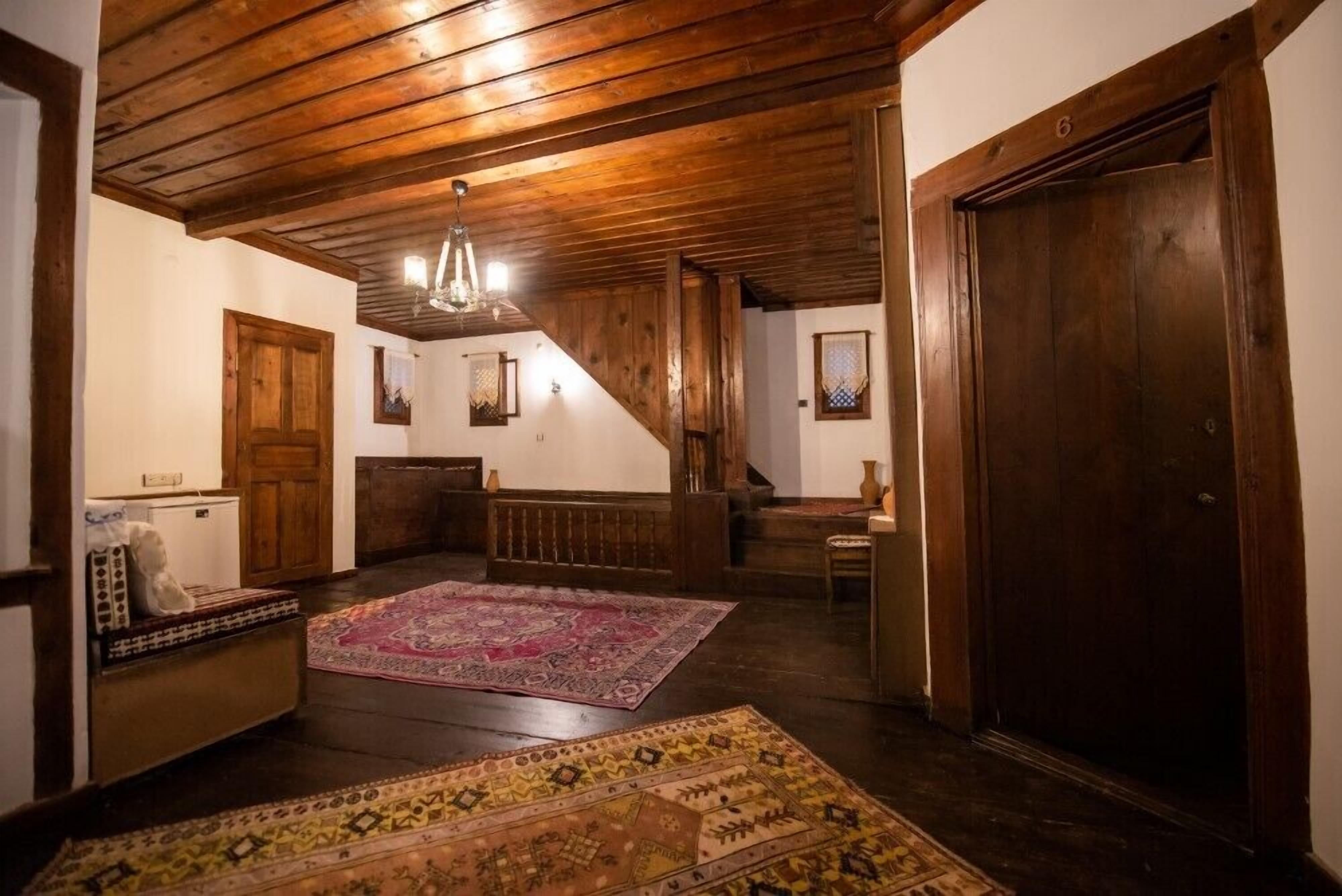A spacious room with wooden beams, a large wooden door, and a staircase leading to another level.