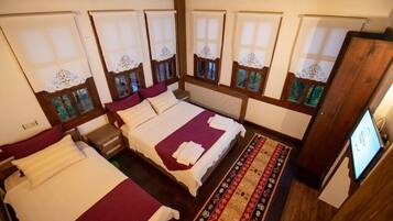 A hotel room with four beds, each with a red and white bedspread, a wooden headboard, and a window with a lace curtain.