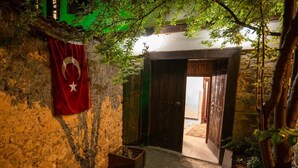 A stone building with a flag, a wooden door, and a small garden area. - Kurkcu Konak (Safranbolu)