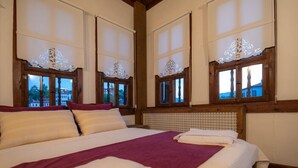 A hotel room with a large bed, wooden headboard, and three windows with decorative curtains. - Kurkcu Konak (Safranbolu)