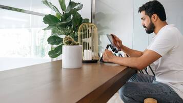A person sitting at a wooden table with a smartphone, a white mug, a potted plant, and a gold cage with a cactus.