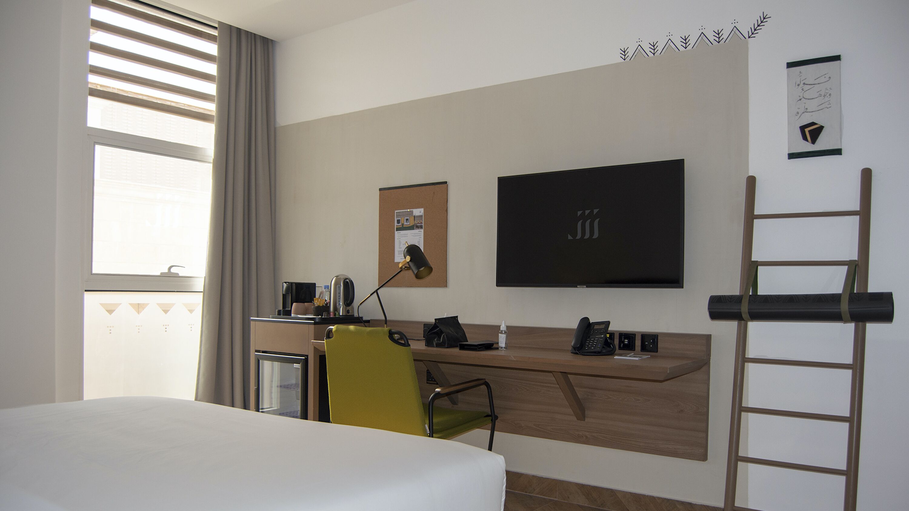Habitación de hotel con cama, escritorio, silla y una ventana grande con persianas.