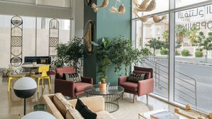 A modern lounge area with round tables, comfortable seating, and large windows offering a view of the street. - Shada Hotel Shatea (Jeddah)
