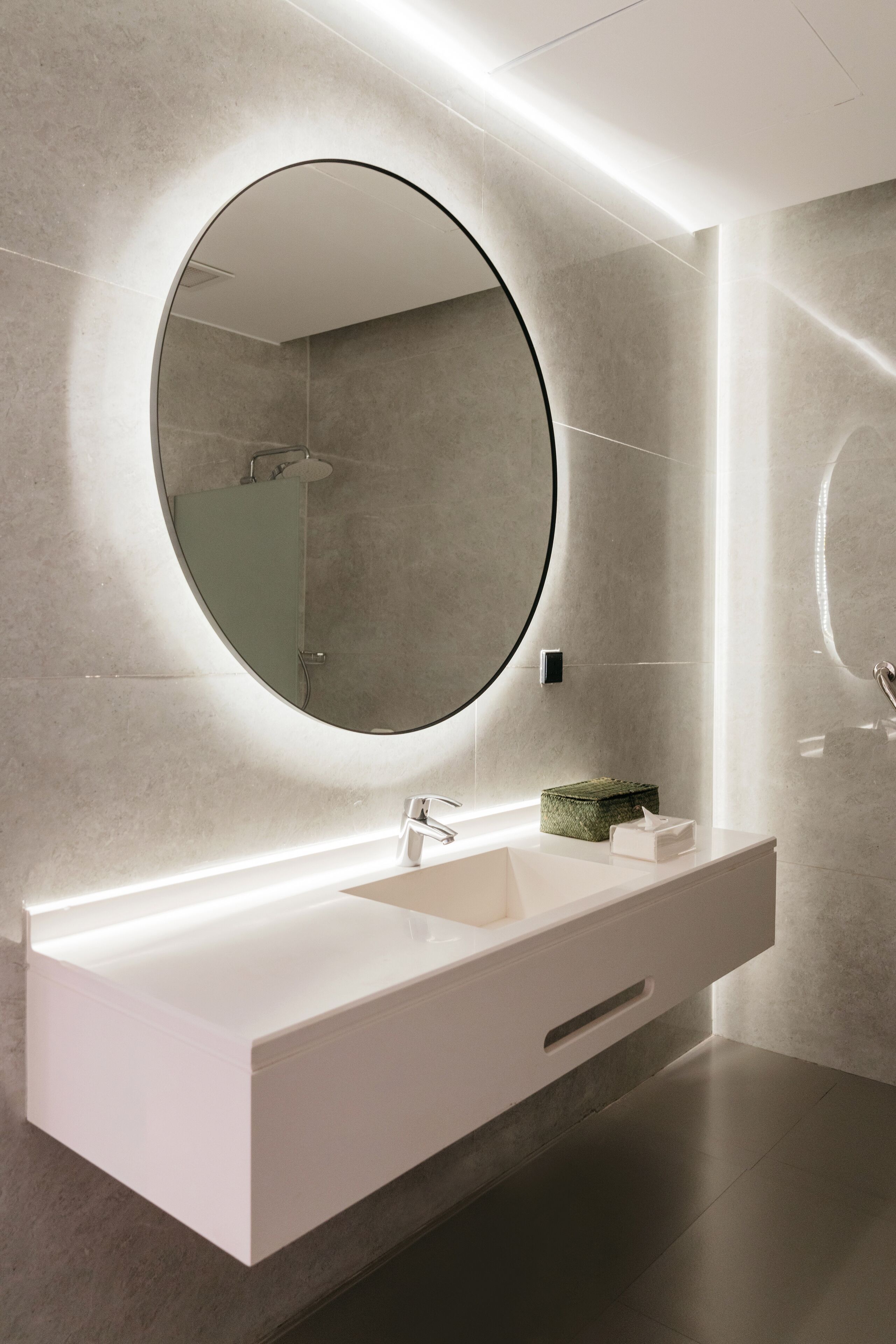 Un bagno moderno con un ampio specchio rotondo, un mobile lavabo bianco e un portasapone verde.