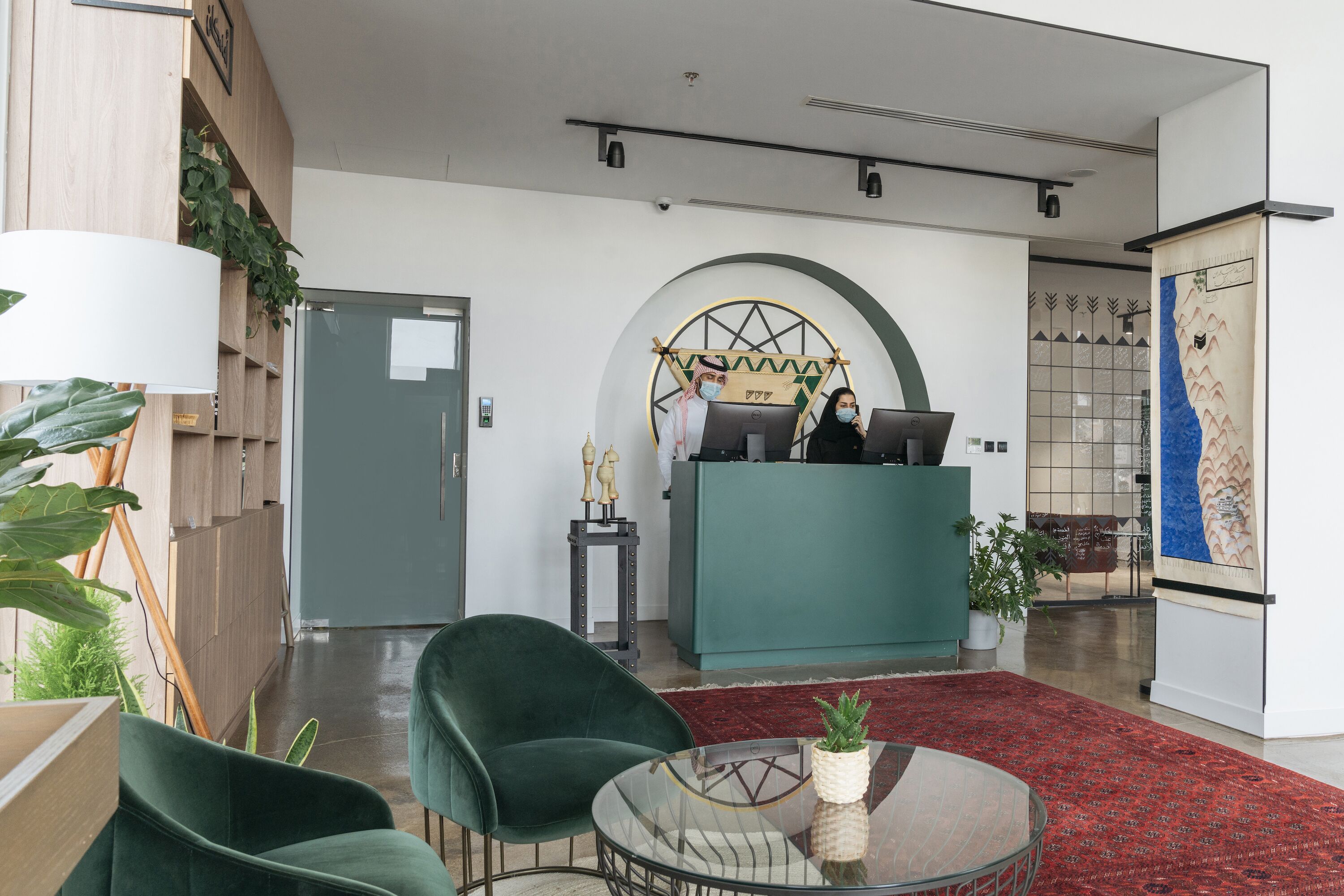 Een moderne receptie met een groen bureau, twee stoelen, een glazen tafel en een rood tapijt.
