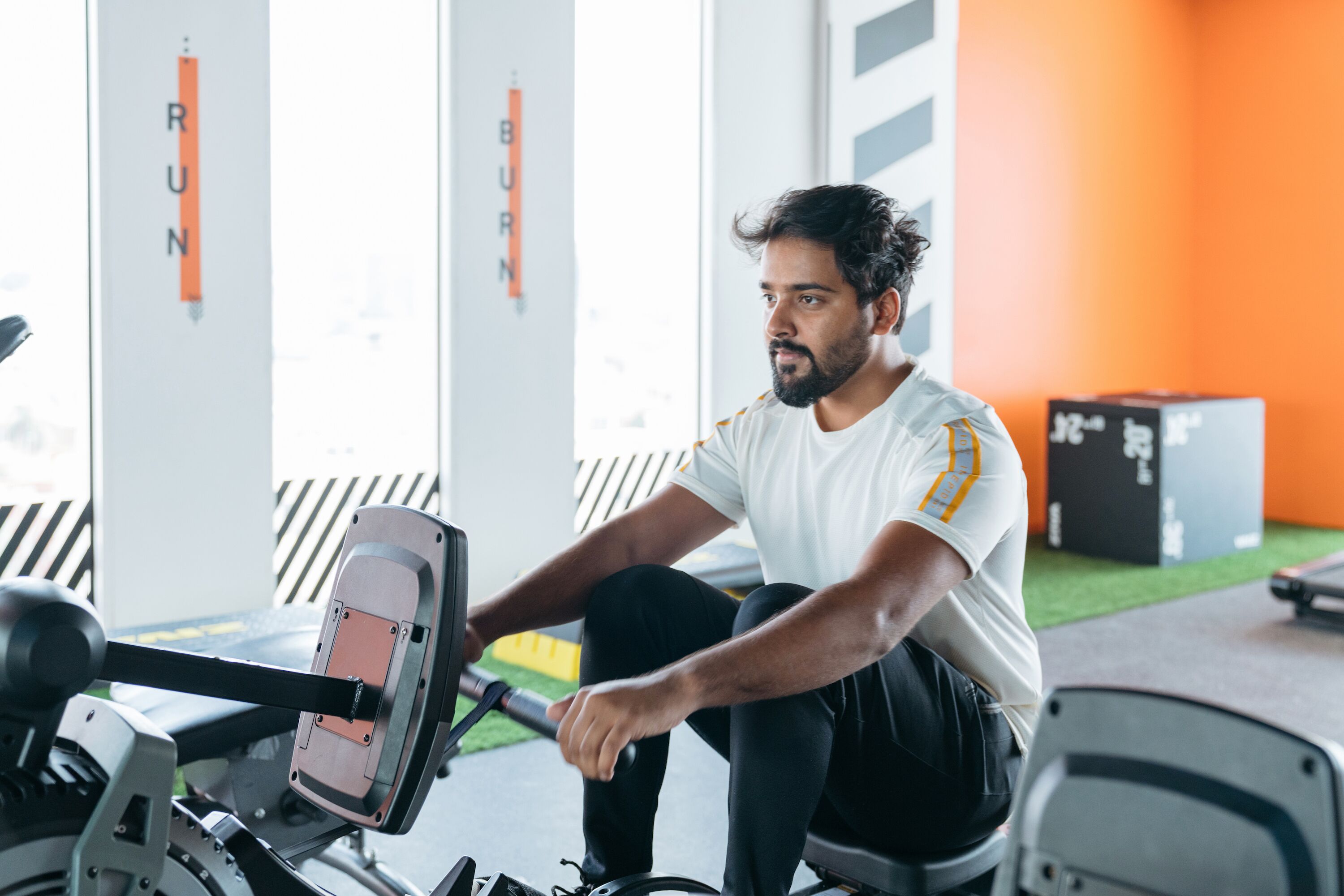 A man using a rowing machine in a gym with orange walls and a window.