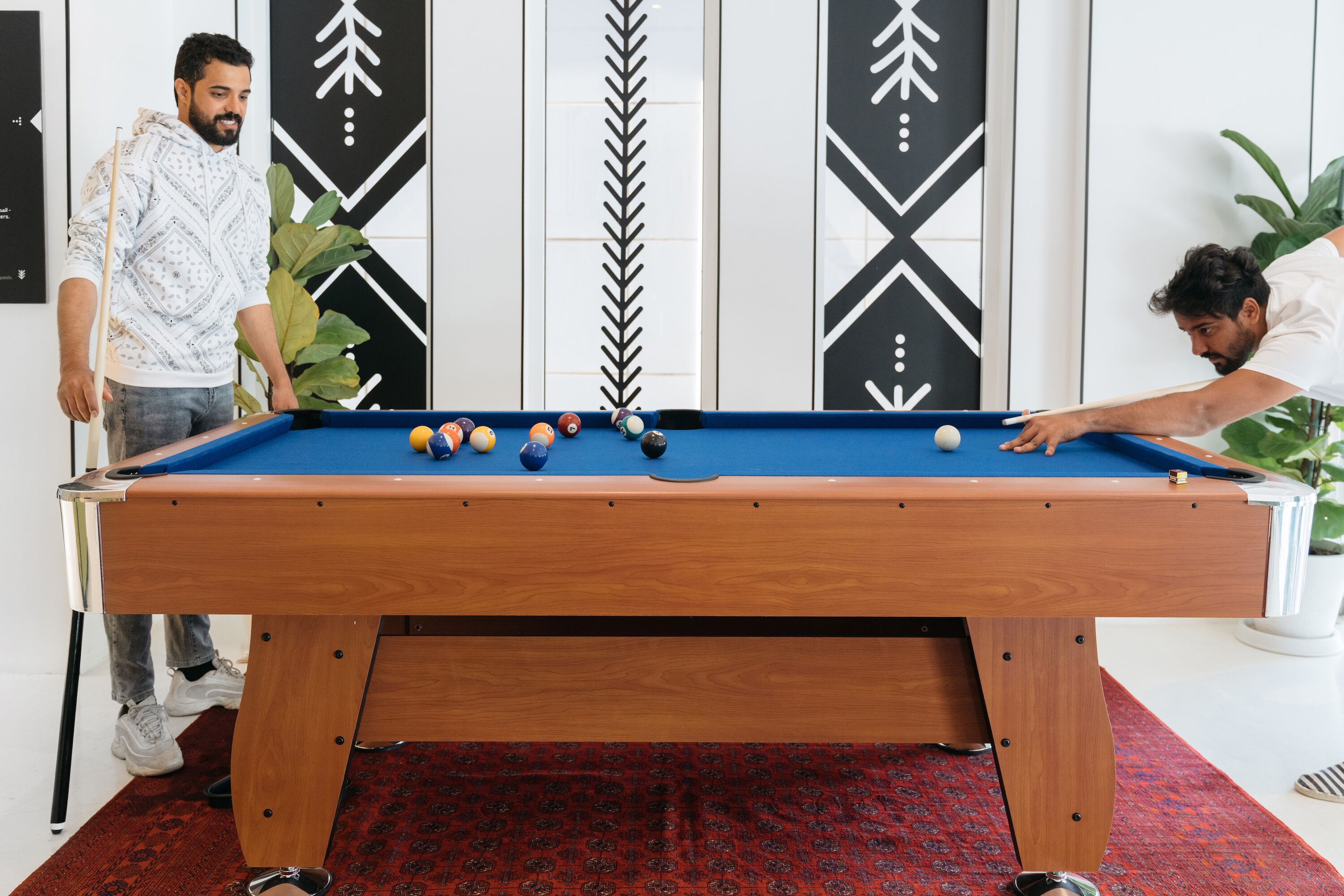 Une table de billard avec des billes, une personne appuyée sur la table et un mur décoratif orné de motifs géométriques.