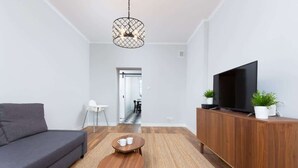 Ett modernt vardagsrum med en grå soffa, ett soffbord i trä, en tv placerad på ett träskåp och en hängande lampa.